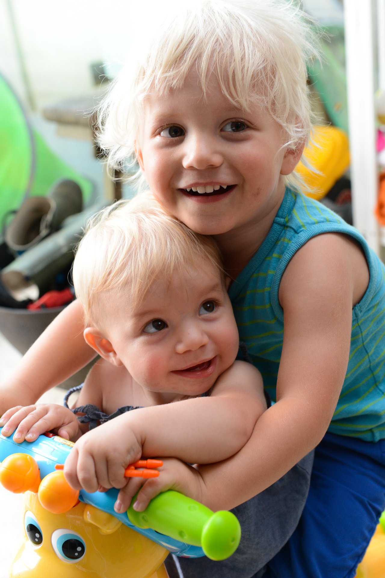 A young child hugs a baby from behind as they sit on a colorful toy ride-on.