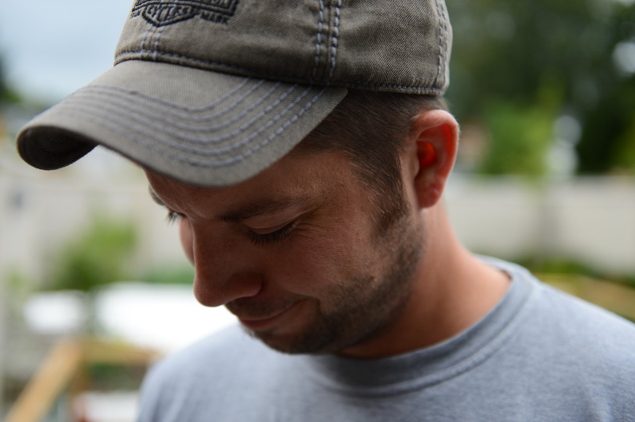 A man wearing a gray cap and shirt looks downward with a slight smile.