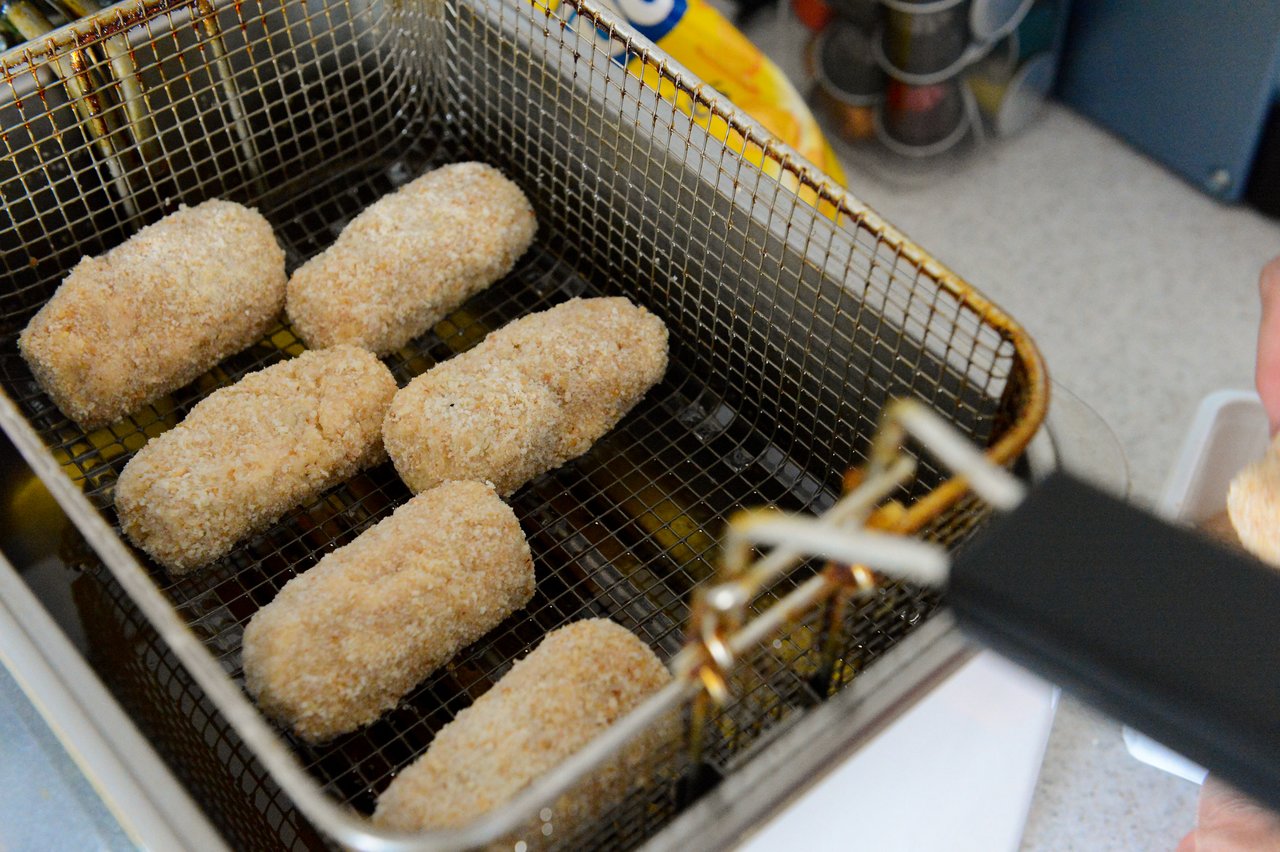 Breaded shrimp croquettes in a deep fryer basket, ready to be cooked.
