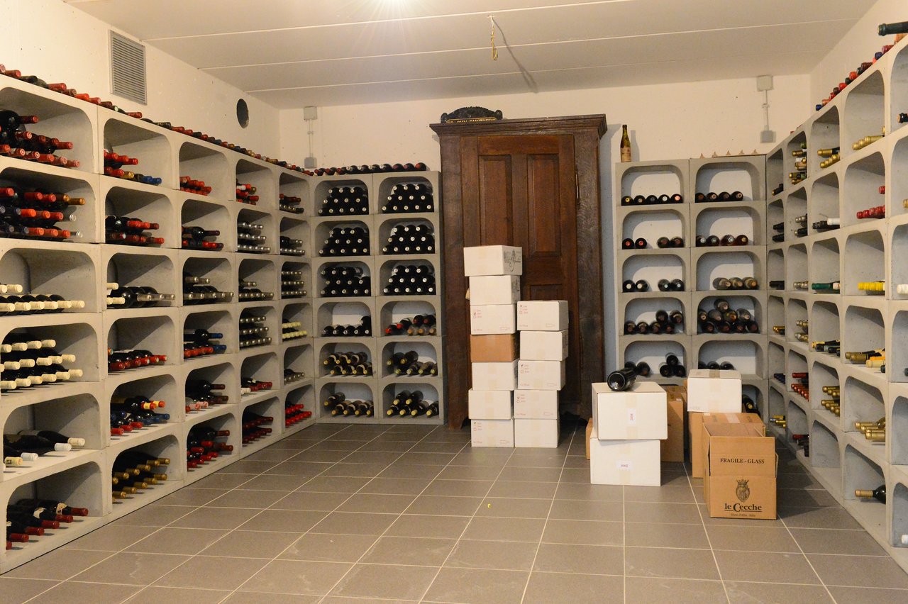 A wine cellar with neatly arranged bottles on shelves and stacked cardboard boxes in the center of the room.