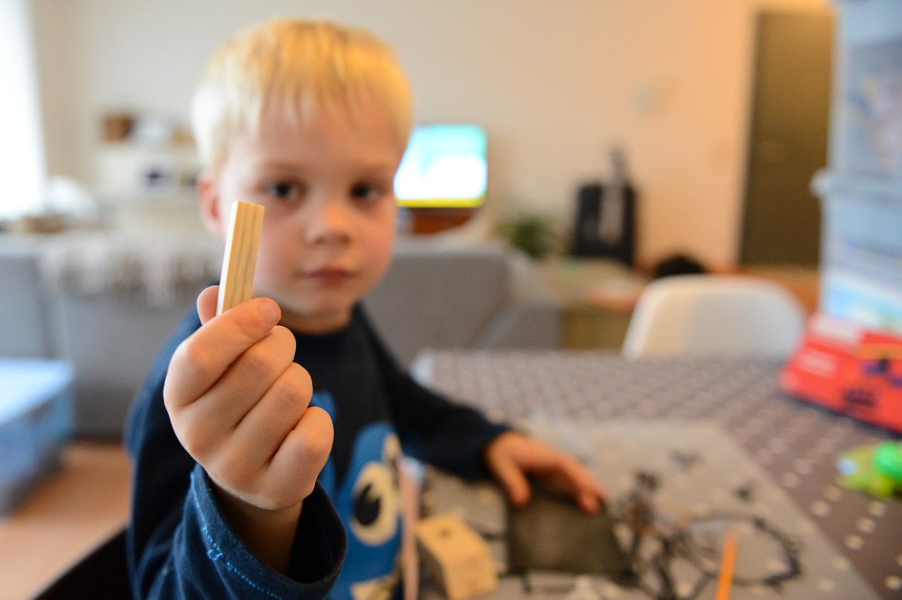 A child holds up a small wooden piece while assembling a helicopter model at a table.