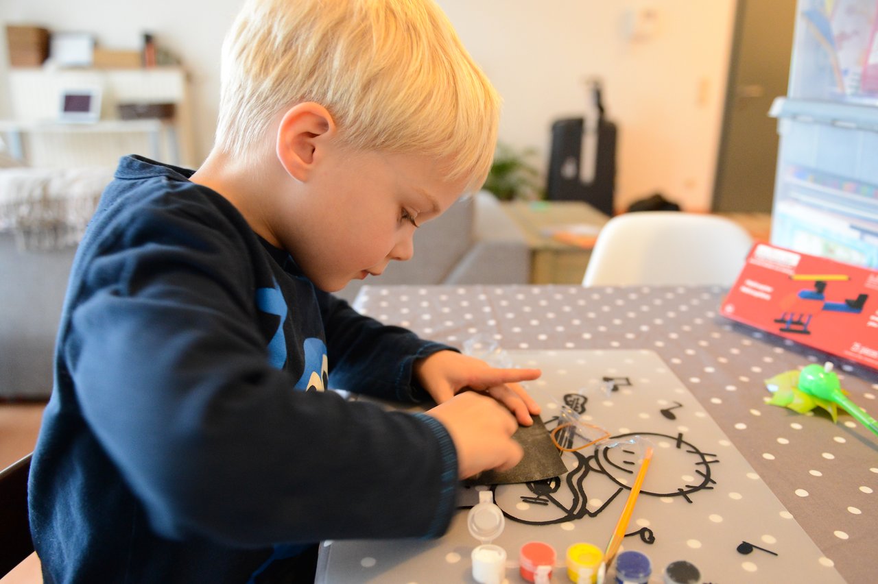 A child is assembling a small helicopter model at a table, using paint and craft materials.