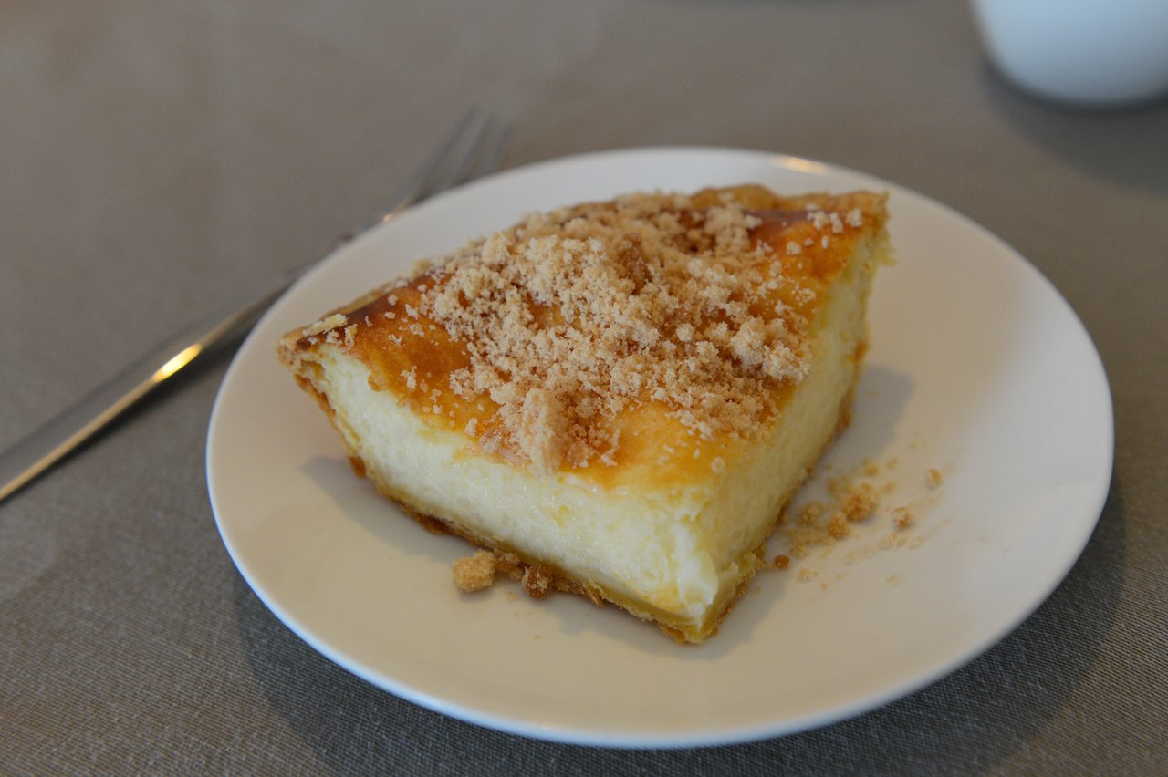 A slice of custard-filled cake with a golden crust and crumb topping on a white plate.