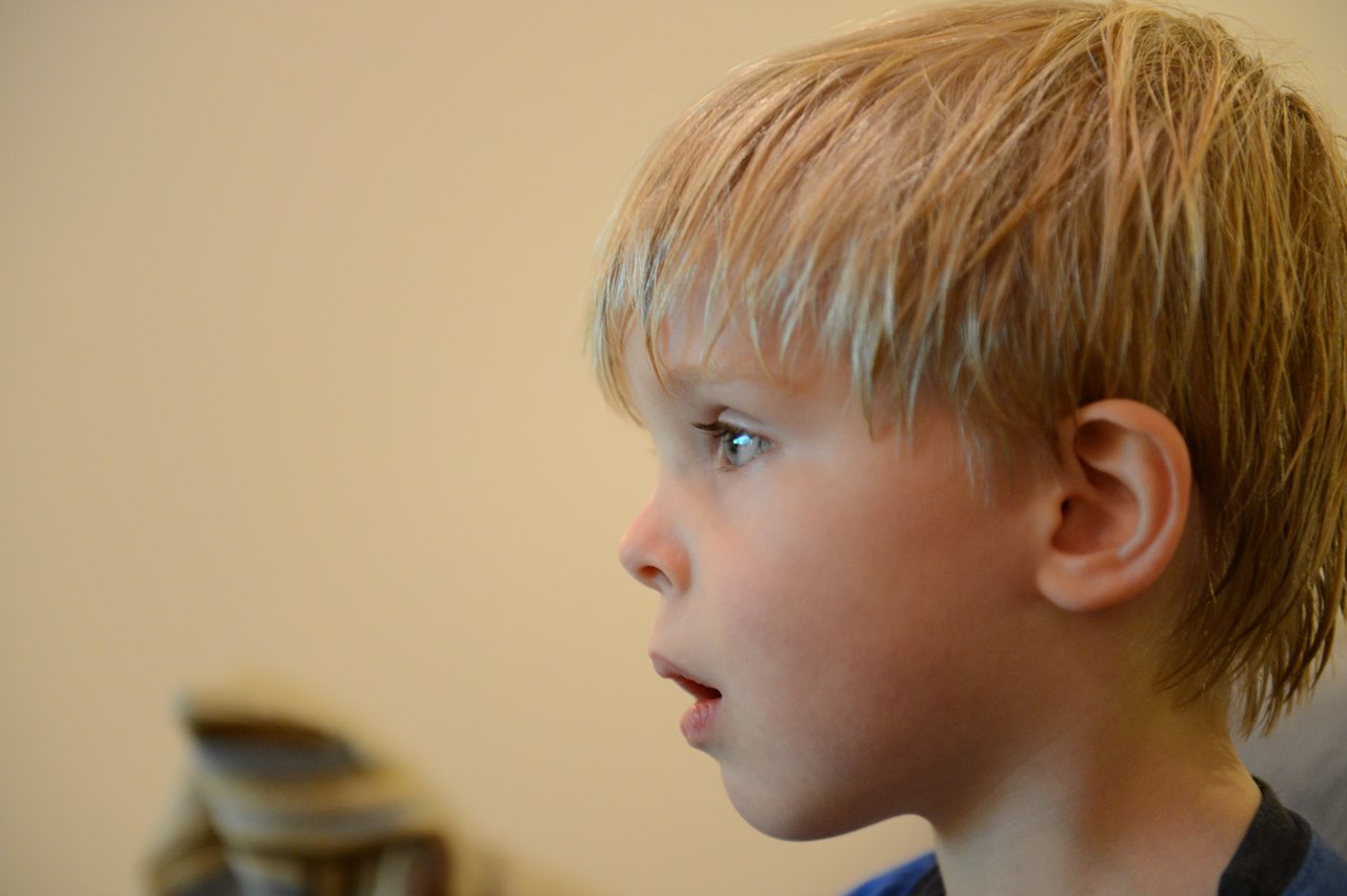 A young child with blond hair watches TV with a focused expression.