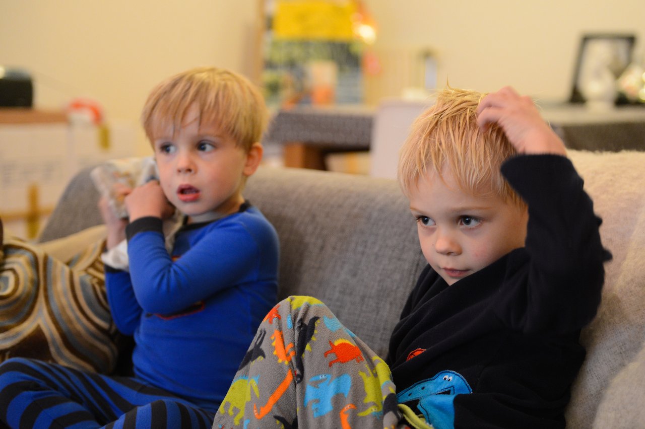 Two young children in pajamas sit on a couch, watching TV with focused expressions.