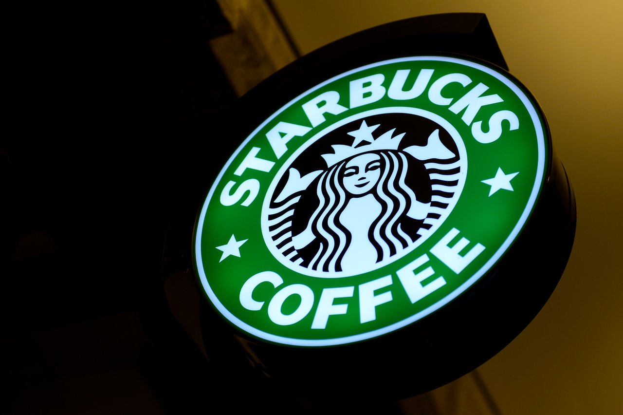 A glowing Starbucks Coffee sign with the company's logo, mounted on a wall at an angle.