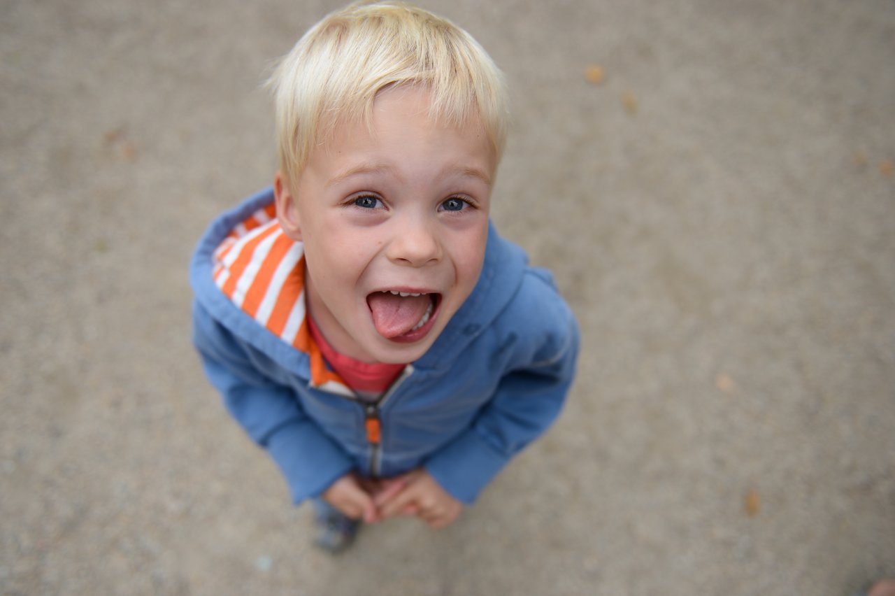 A young child in a blue hoodie sticks out their tongue while looking up at the camera.