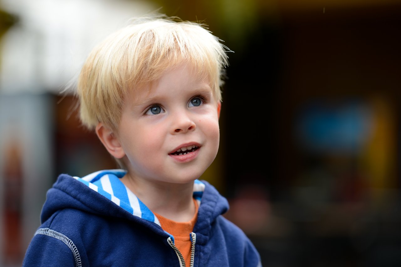 A young child with blond hair and a blue hoodie looks up with a curious expression.