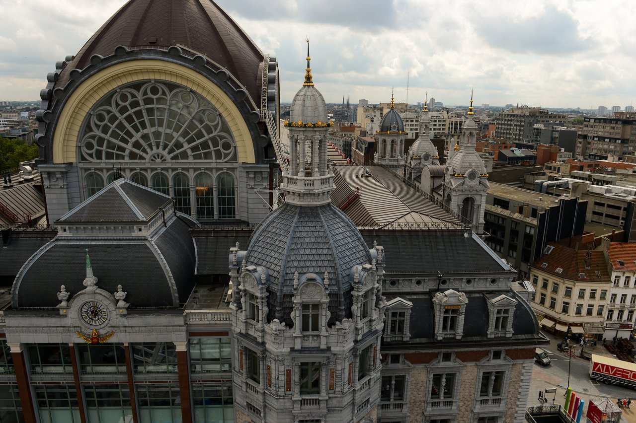 A Ferris wheel view overlooking the ornate architecture of Antwerp Central Station with the cityscape in the background.