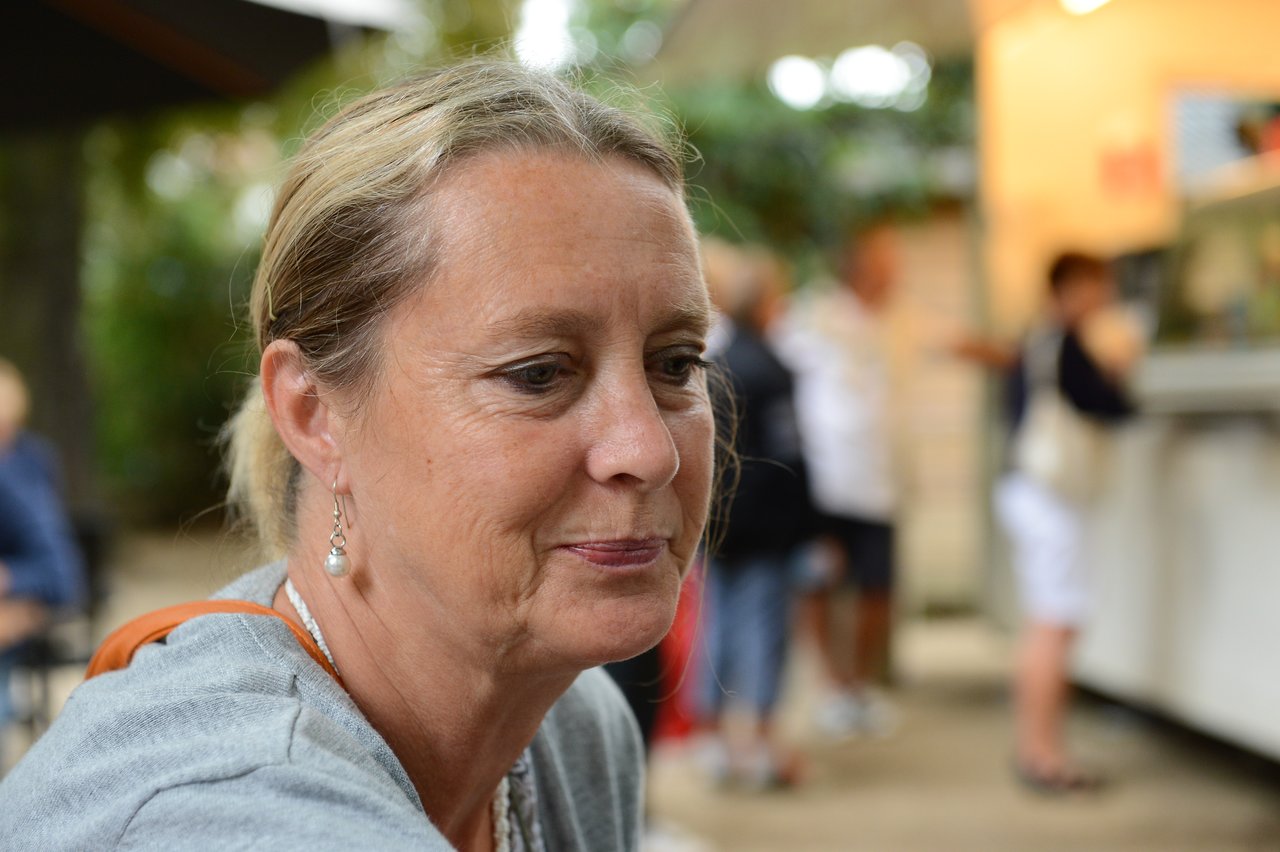 A woman with a gentle smile looks down, wearing earrings and a light sweater.