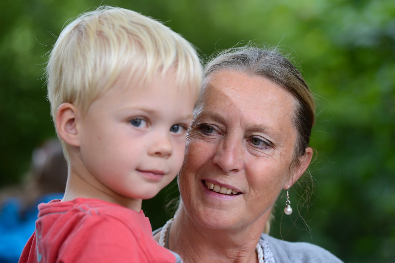 An older woman smiles while looking at a young boy with blonde hair, who is gazing at the camera.