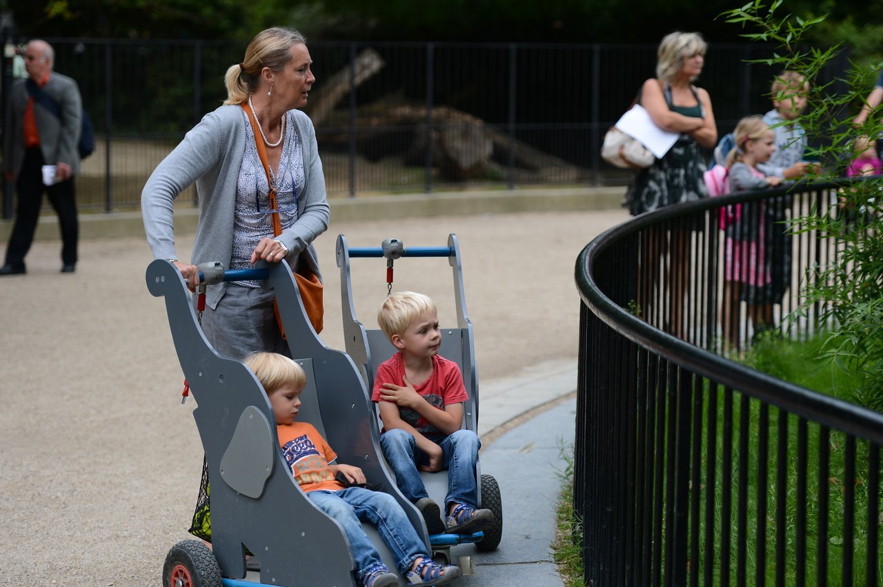 A woman pushes a stroller with two young children as they look at an animal enclosure at the zoo.