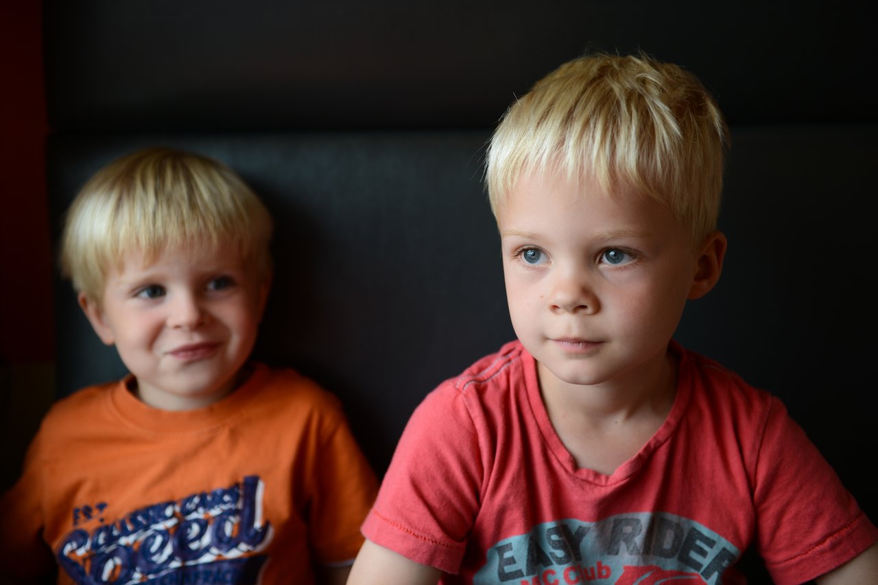 Two young children sit on a train, one looking serious while the other smiles slightly.