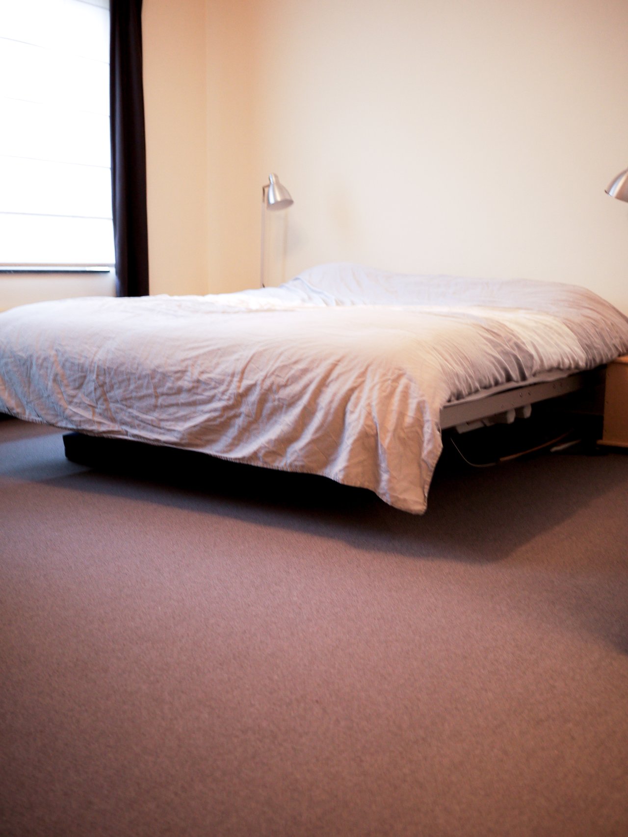 A bedroom with a large bed, white bedding, two bedside lamps, and a window with curtains.