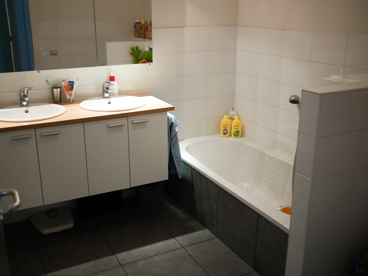 A bathroom with a double sink vanity, a bathtub with toiletries, and a mirror reflecting the space.