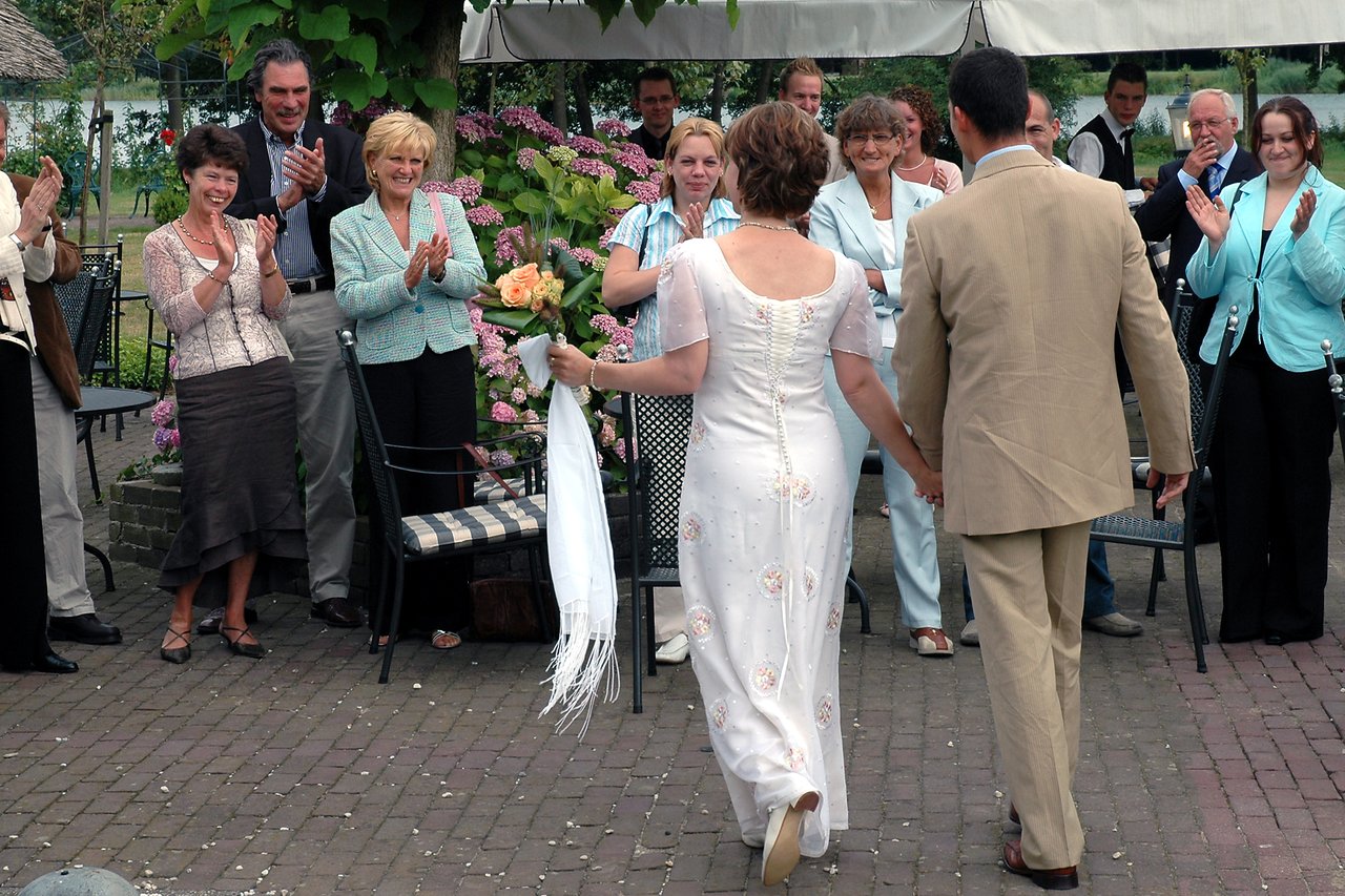 A bride and groom walk hand in hand as guests applaud their entrance at an outdoor wedding gathering.