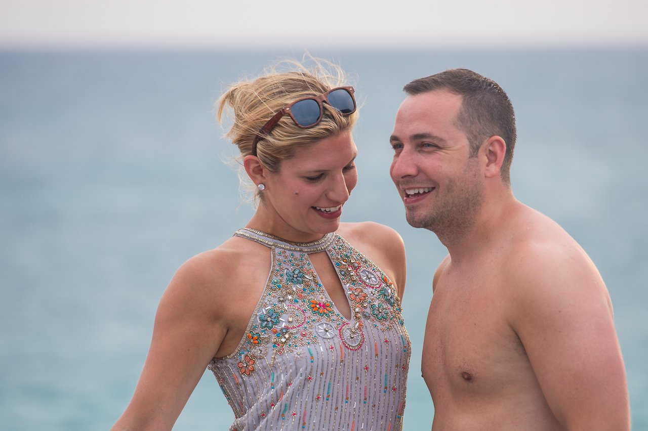 A smiling man and woman stand close together near the water, enjoying a moment at a boat party.