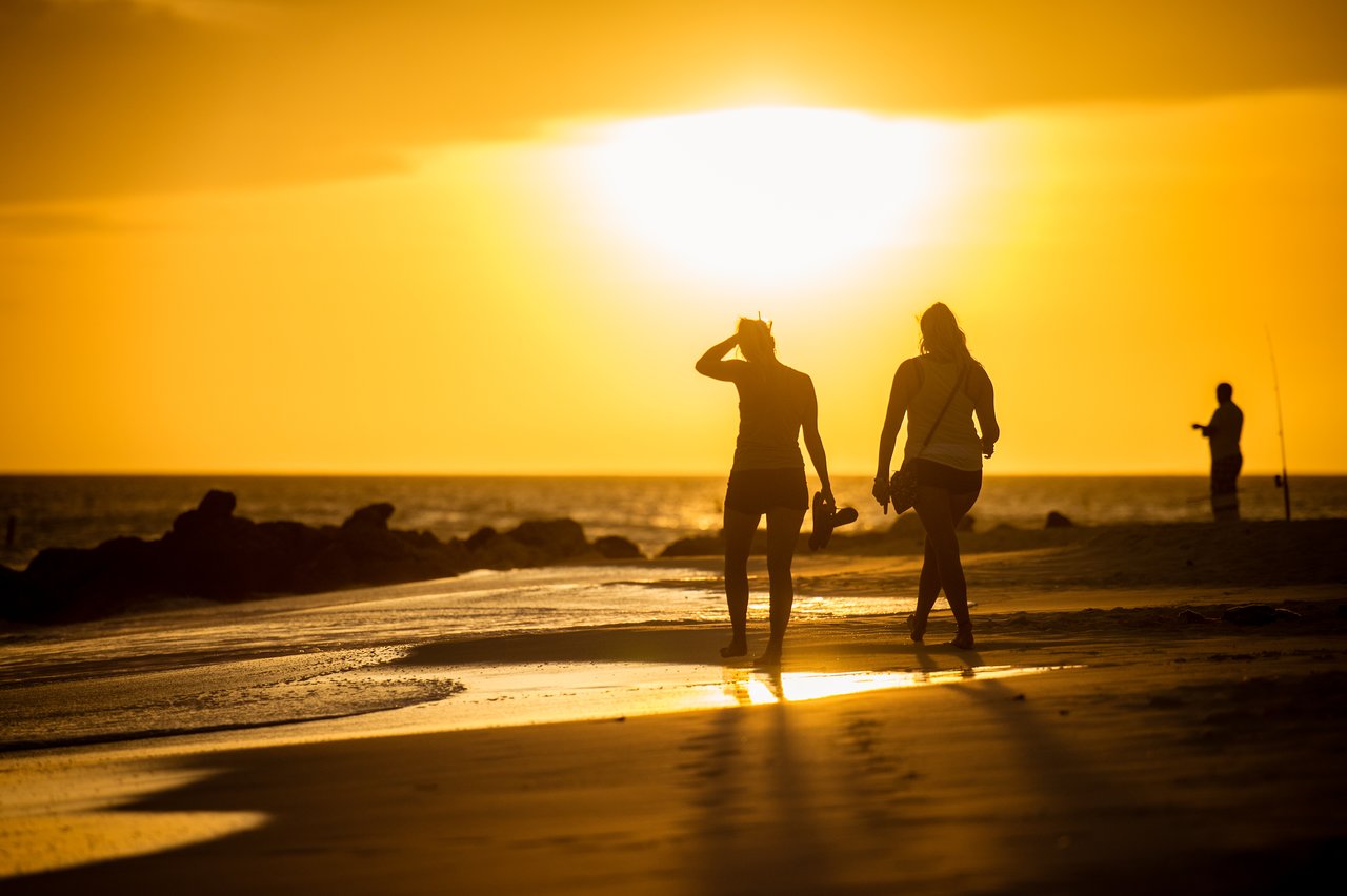 Two friends walk along the beach at sunset, holding their shoes.