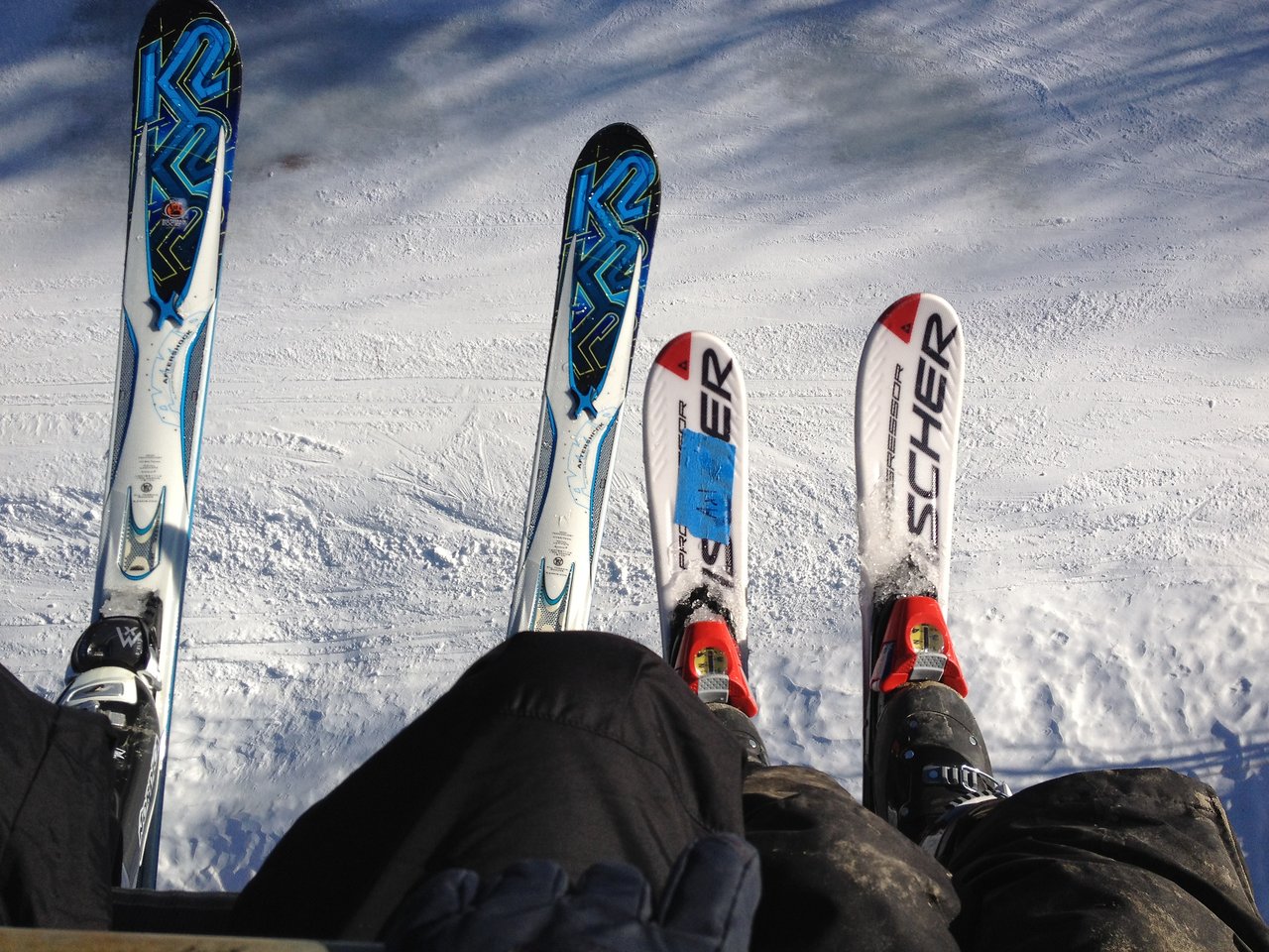Two people sitting on a ski lift with their skis dangling above the snowy ground.