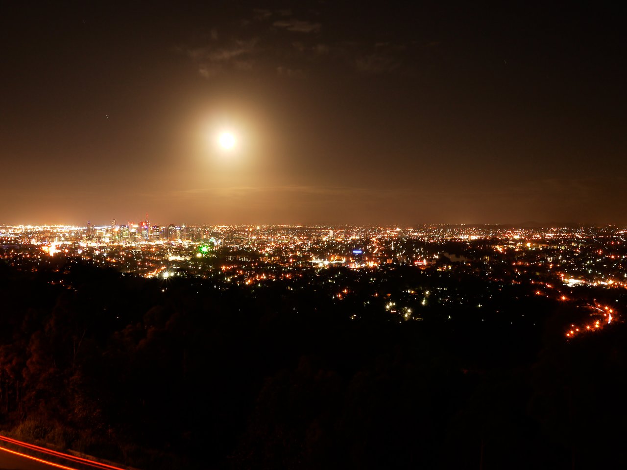 A nighttime view of Brisbane with city lights glowing under a bright full moon in the sky.