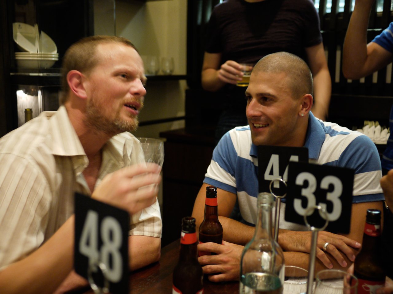 Two men sit at a table with drinks, engaged in conversation during a Brisbane Drupal meetup.