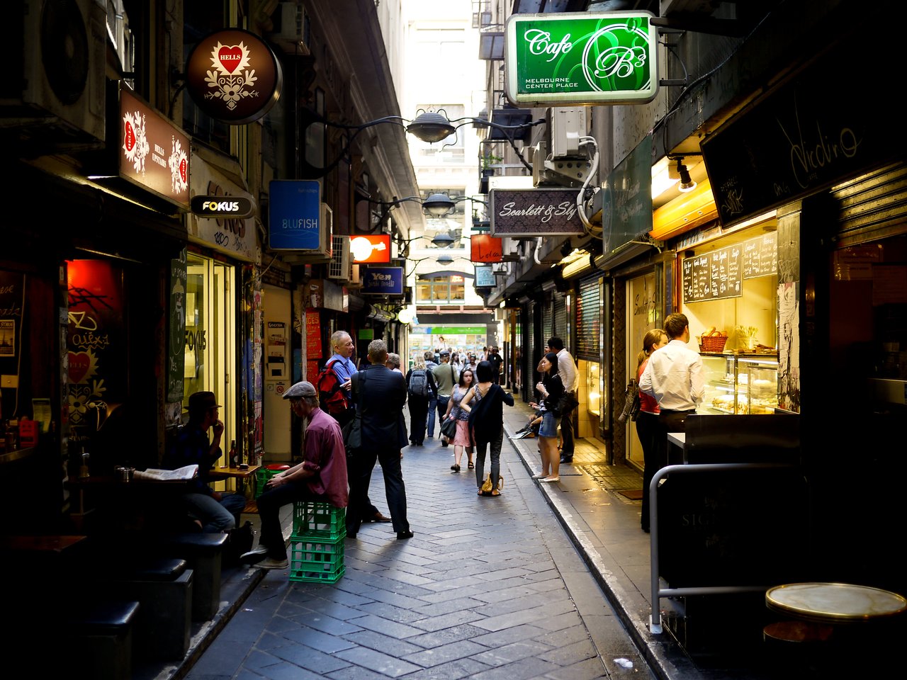 A narrow Melbourne laneway with people sitting and standing outside cafes, ordering food, and walking through.