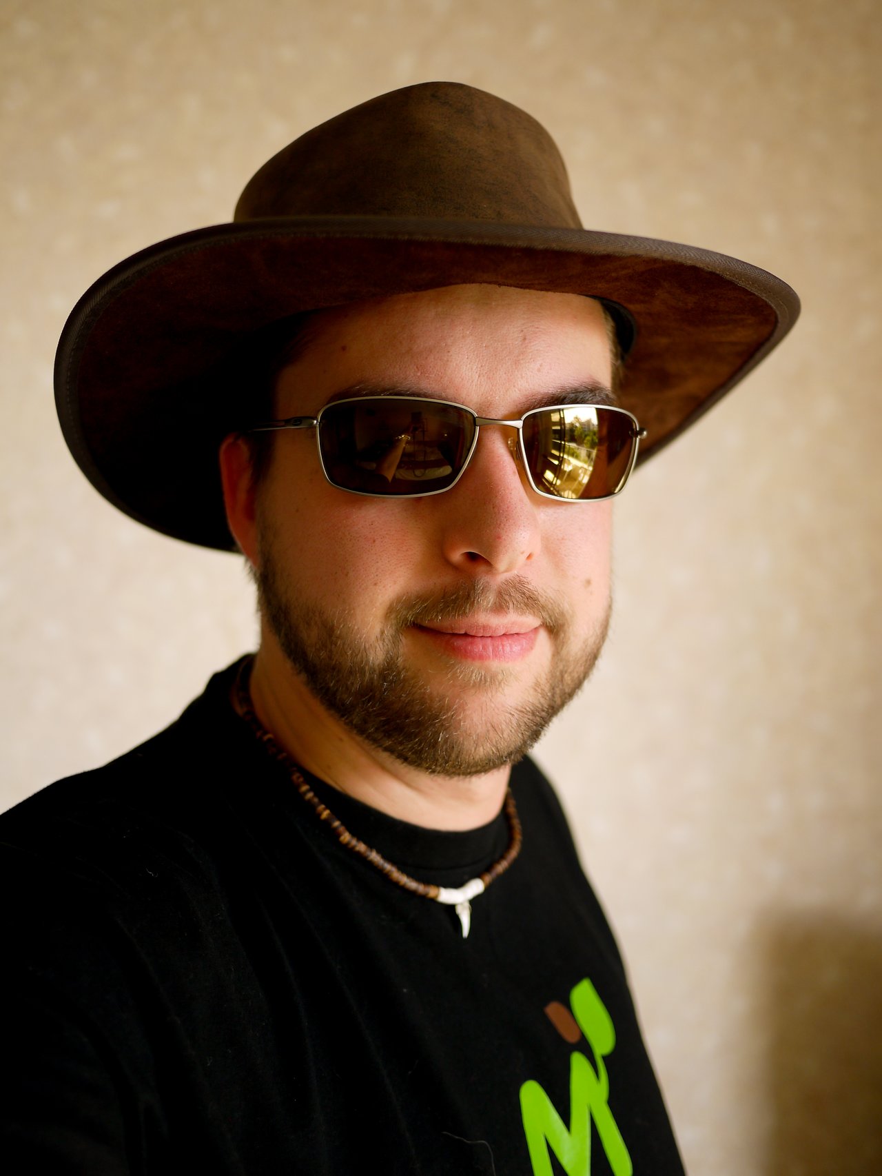 A person wearing a brown hat with crocodile teeth, sunglasses, and a necklace with a crocodile tooth.