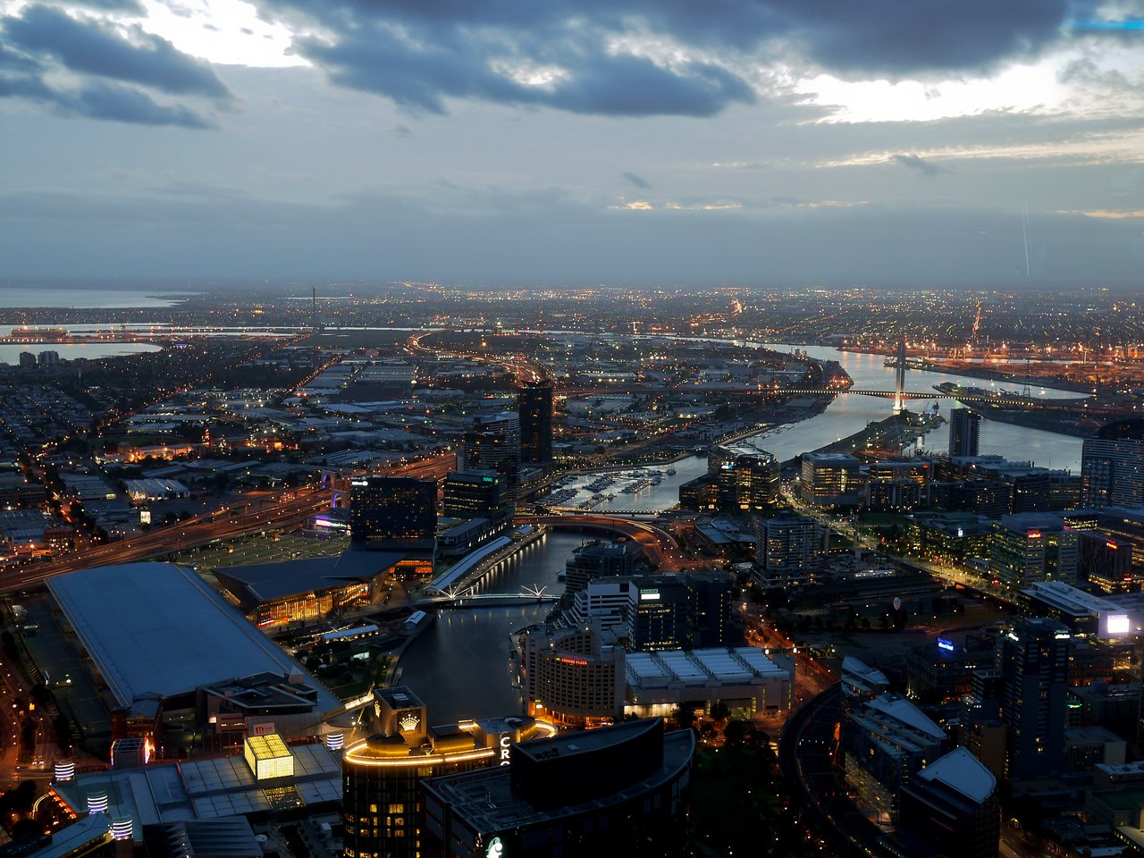 Aerial view of Melbourne at night, showing illuminated buildings, roads, and a river reflecting city lights.