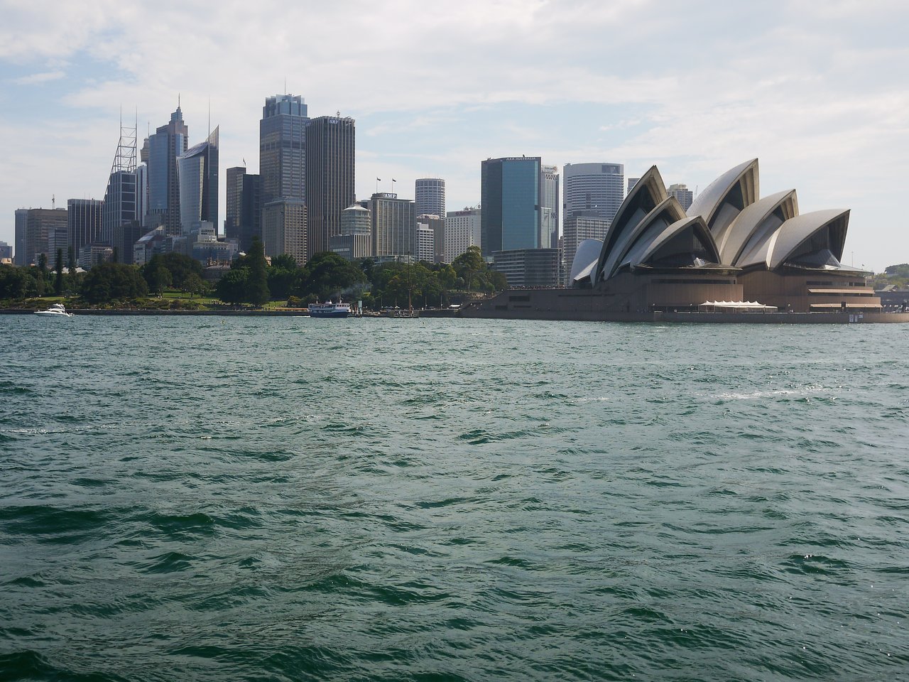 Sydney skyline with modern high-rise buildings and the Sydney Opera House, viewed from across the water.