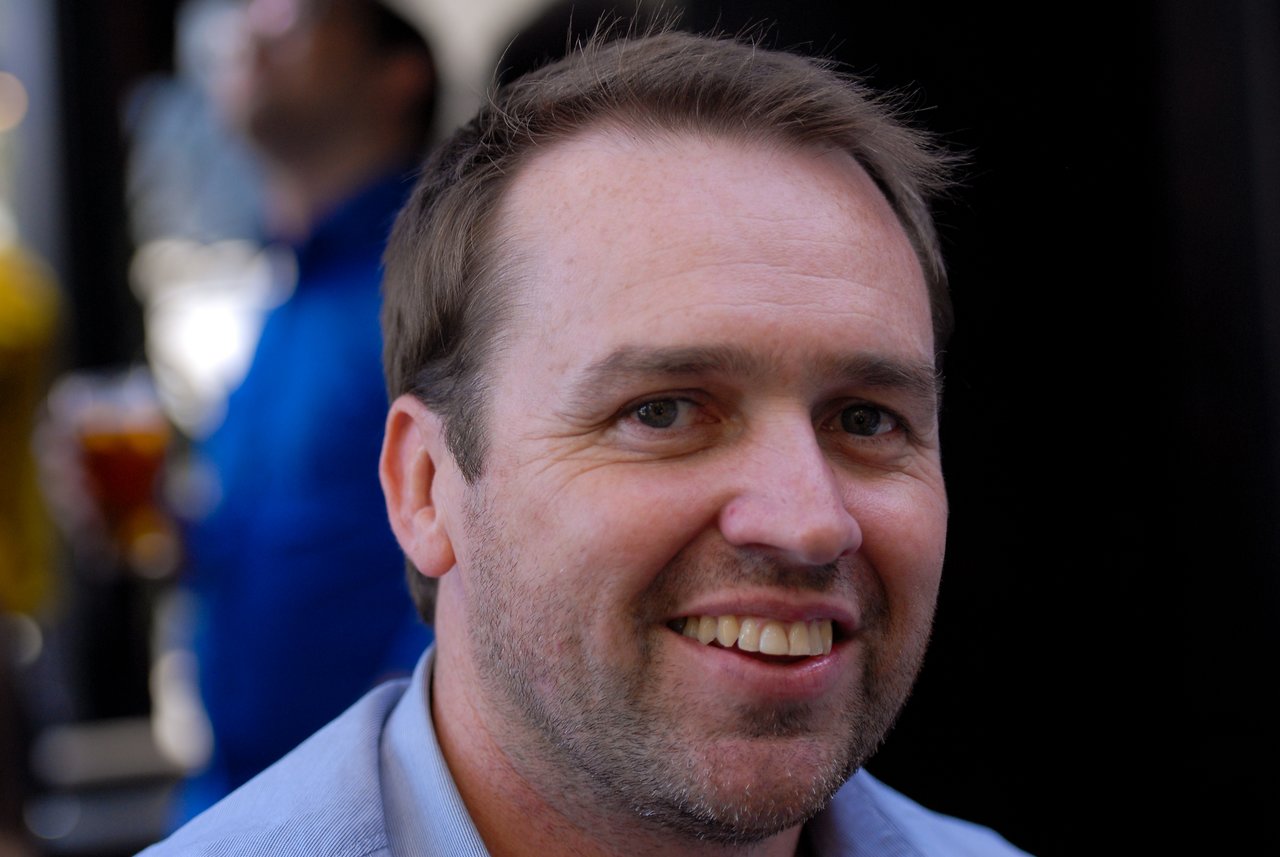 A man with short brown hair and a beard smiles at the camera.