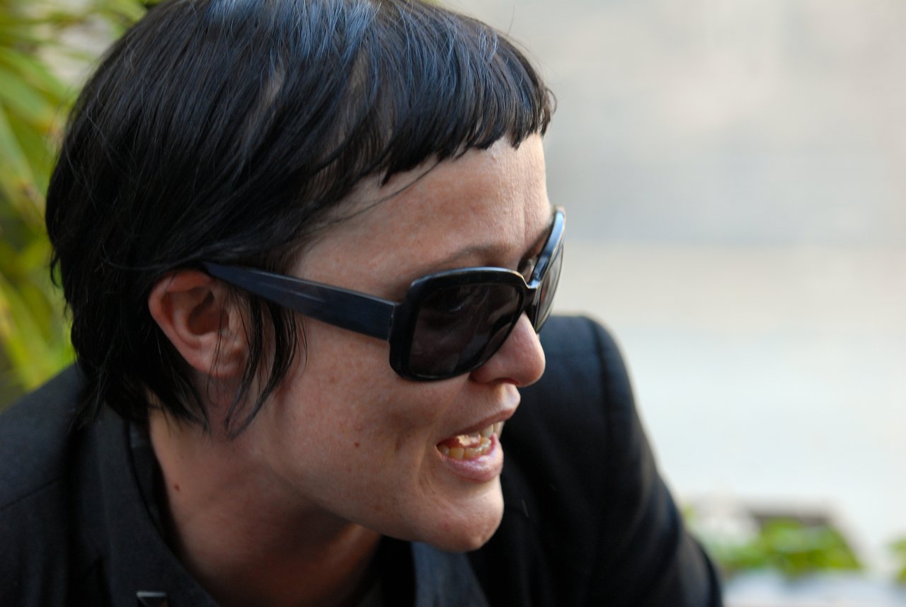 A person wearing sunglasses and a black outfit is talking at a party, appearing engaged in conversation.