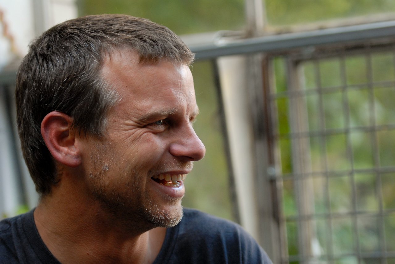A man with short hair and a beard smiles while looking to the side at a party.
