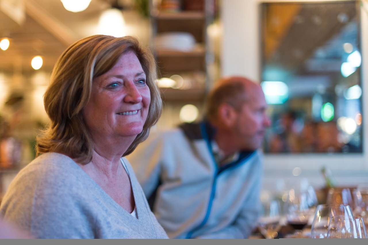 A woman in a light sweater smiles while sitting at a table.