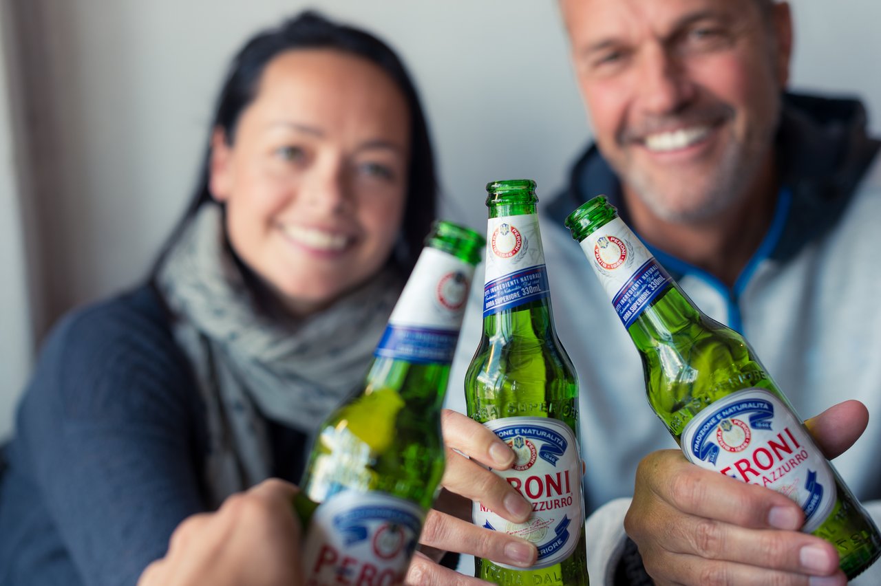 Three people clink their beer bottles together in a toast, smiling and enjoying a moment together.