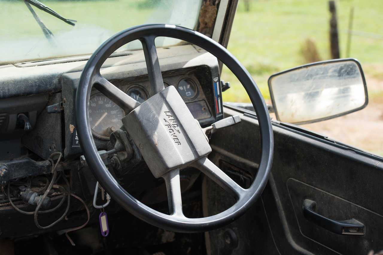 Close-up of a worn Land Rover steering wheel and dashboard in a dusty, aging interior.