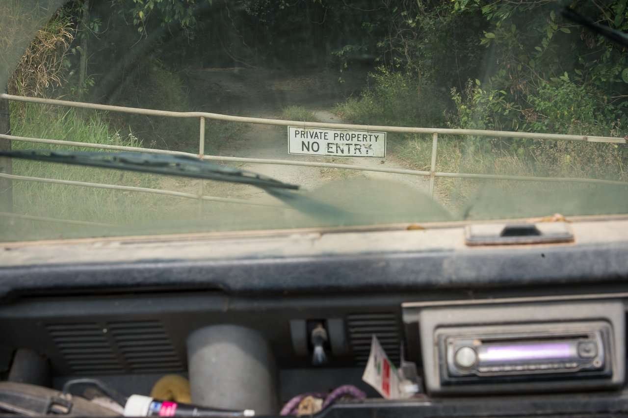 A metal gate with a "Private property - no entry" sign blocks a dirt road, viewed from inside a vehicle.