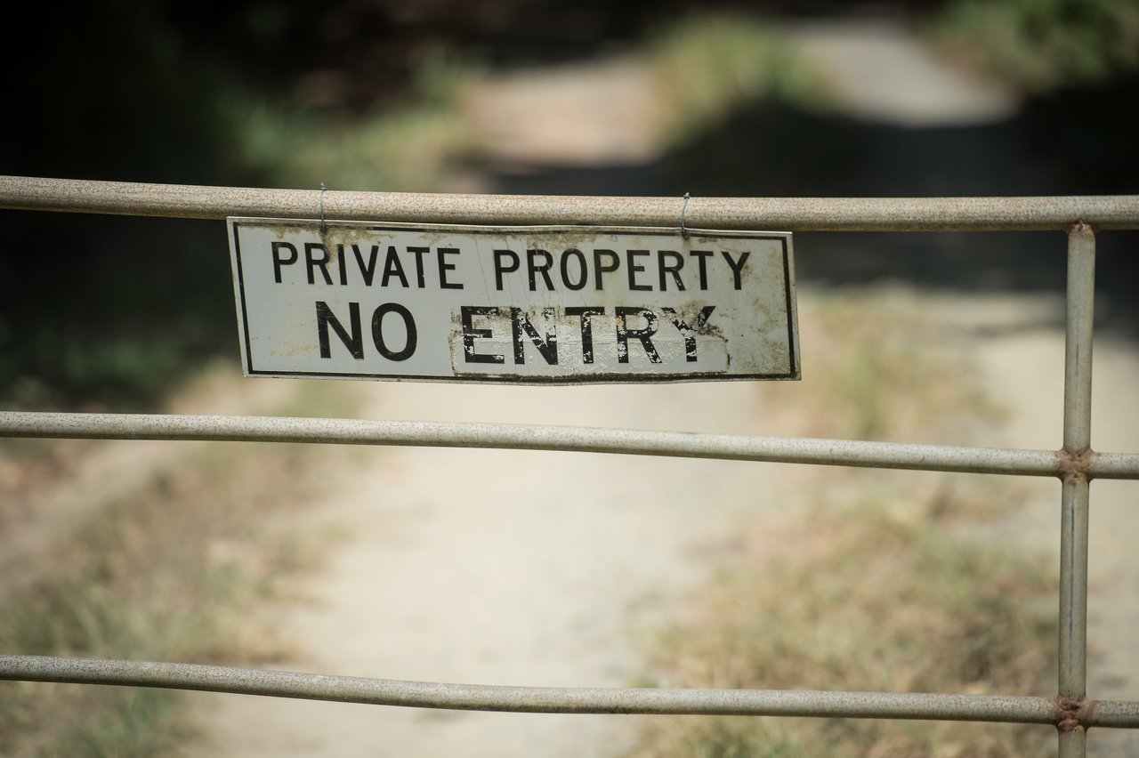 A weathered "Private Property - No Entry" sign is attached to a metal gate blocking a dirt path.