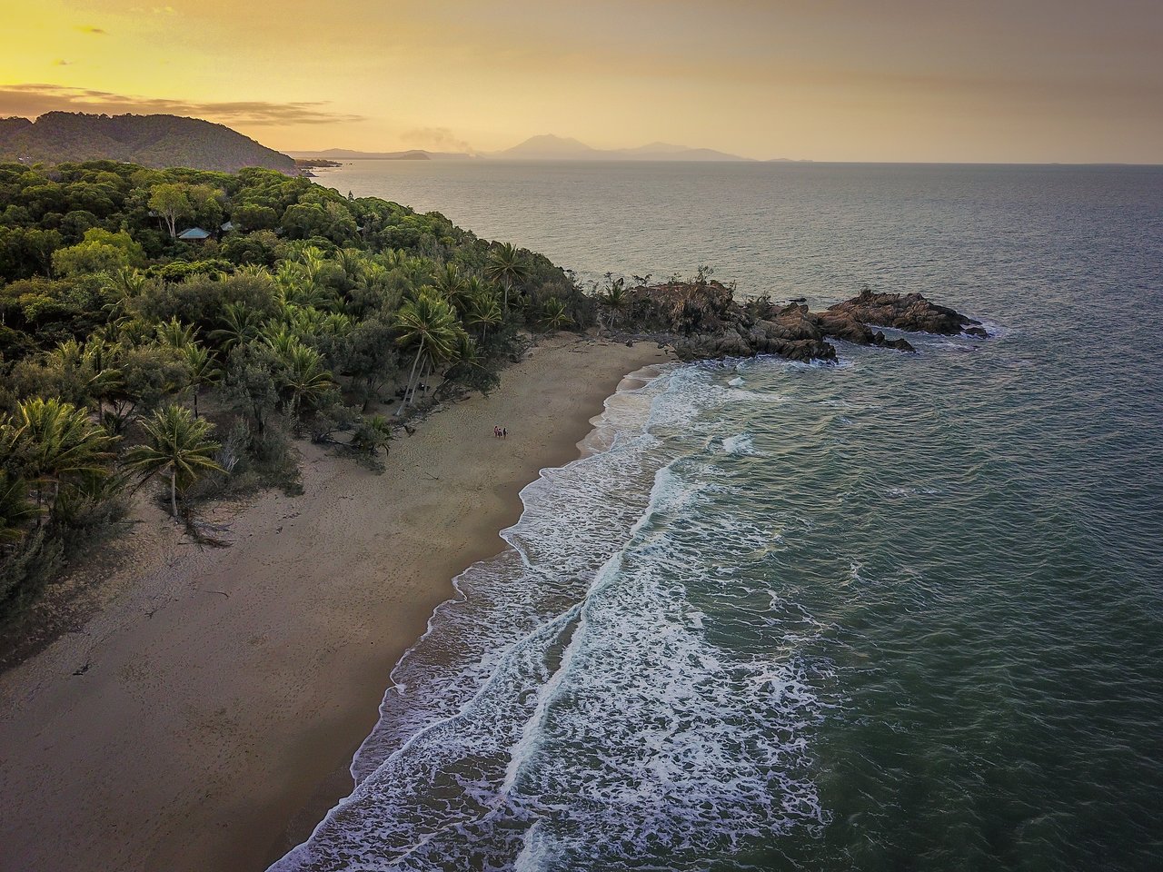 A sandy beach with ocean waves, surrounded by green trees.