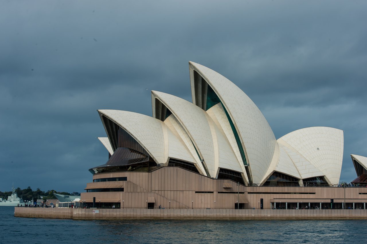 The Sydney Opera House with its white sail-like roofs stands by the water.