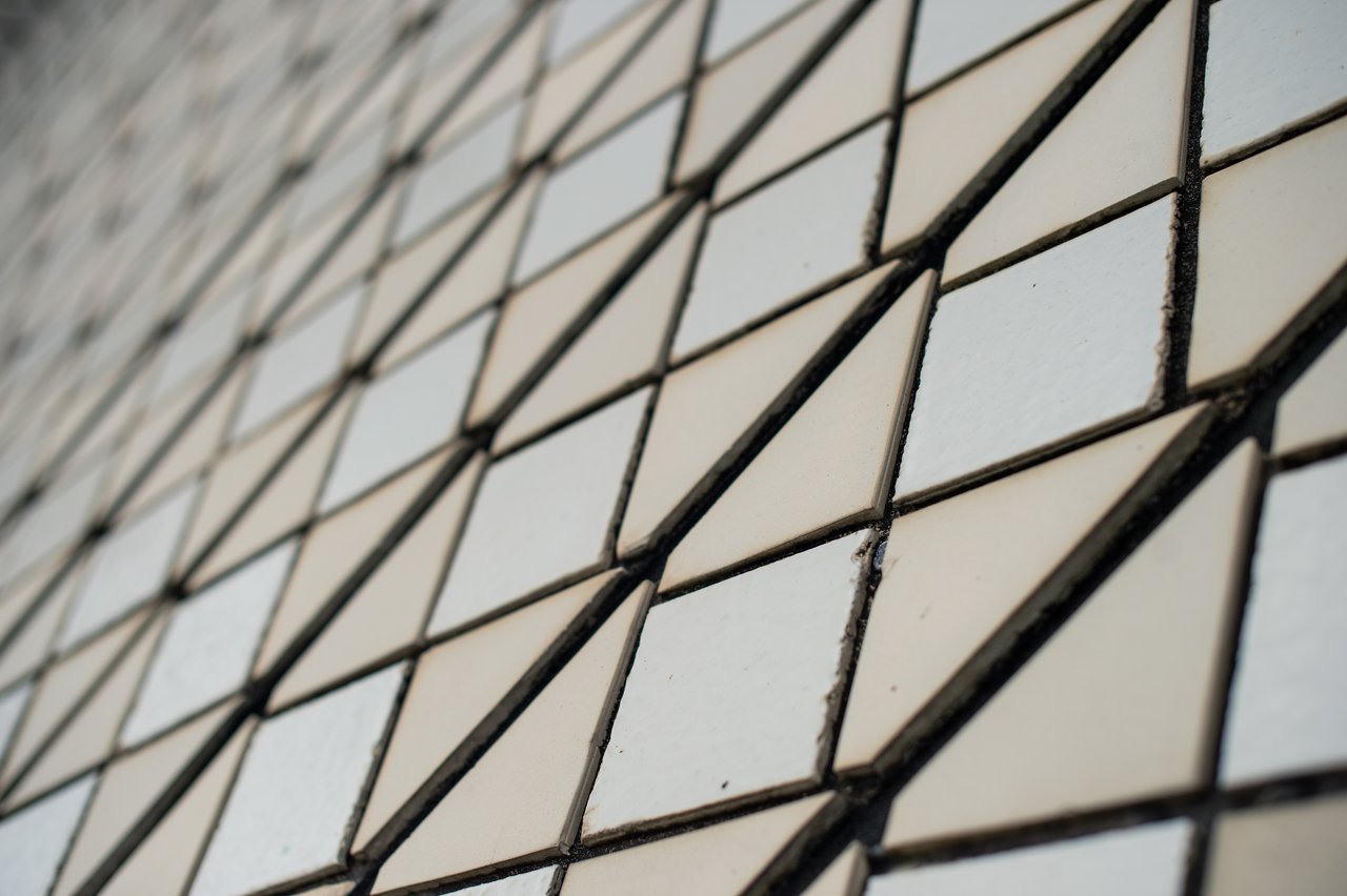 Close-up of the Sydney Opera House's tiled surface, showcasing its iconic geometric pattern of white and beige triangular tiles, separated by dark grout lines.