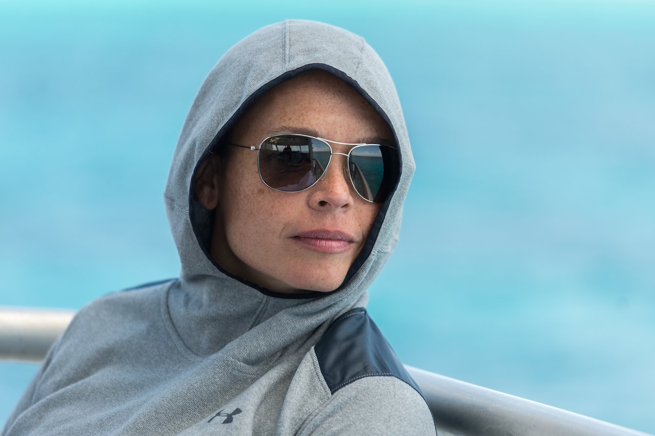 A woman wearing a gray hoodie and sunglasses looks off to the side with a calm expression.