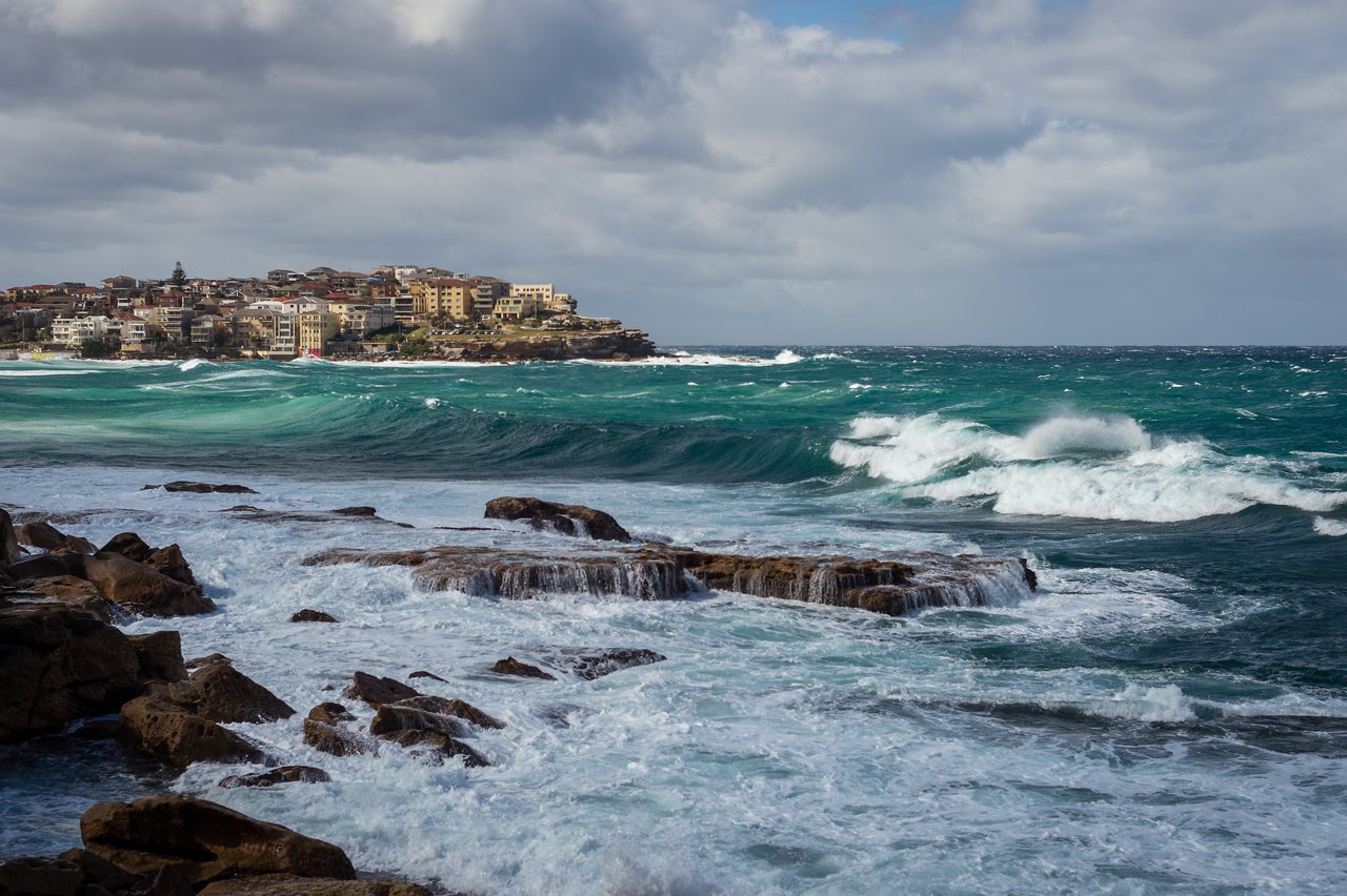 Waves crash against rocky shoreline with ocean water flowing over the rocks.