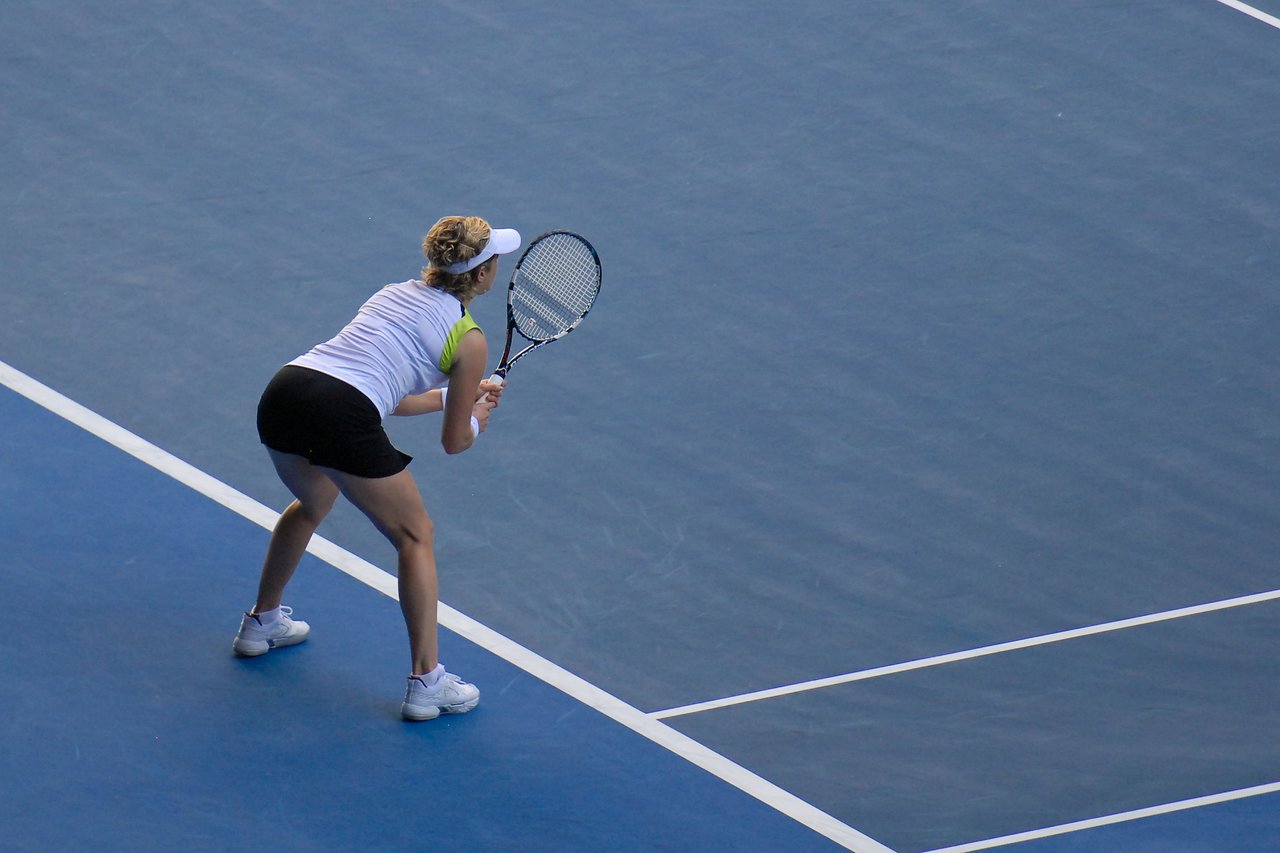 A tennis player in a ready position, holding a racket, preparing to receive a serve on a blue court.