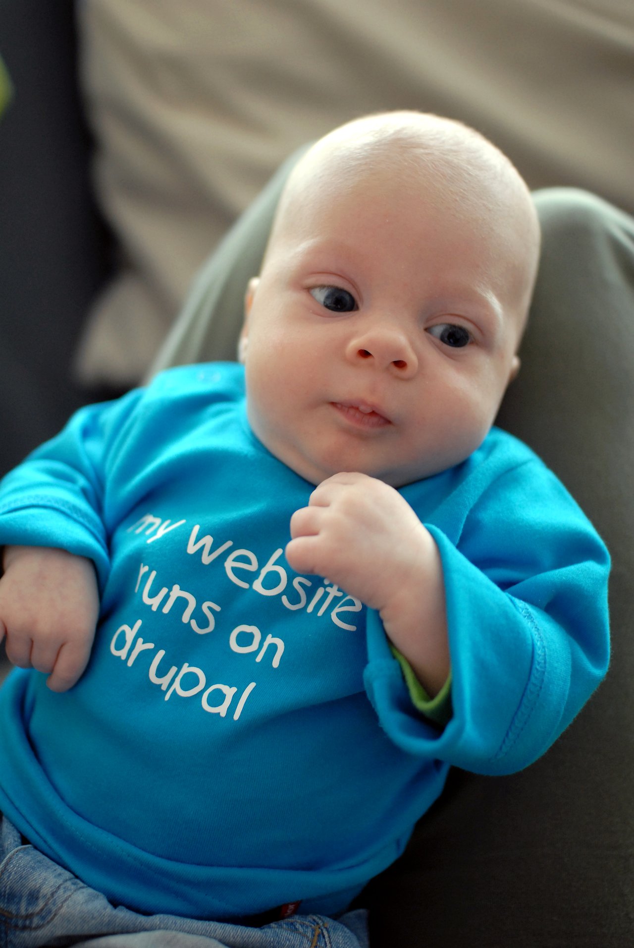 A baby wearing a blue shirt with the text "My website runs on Drupal".