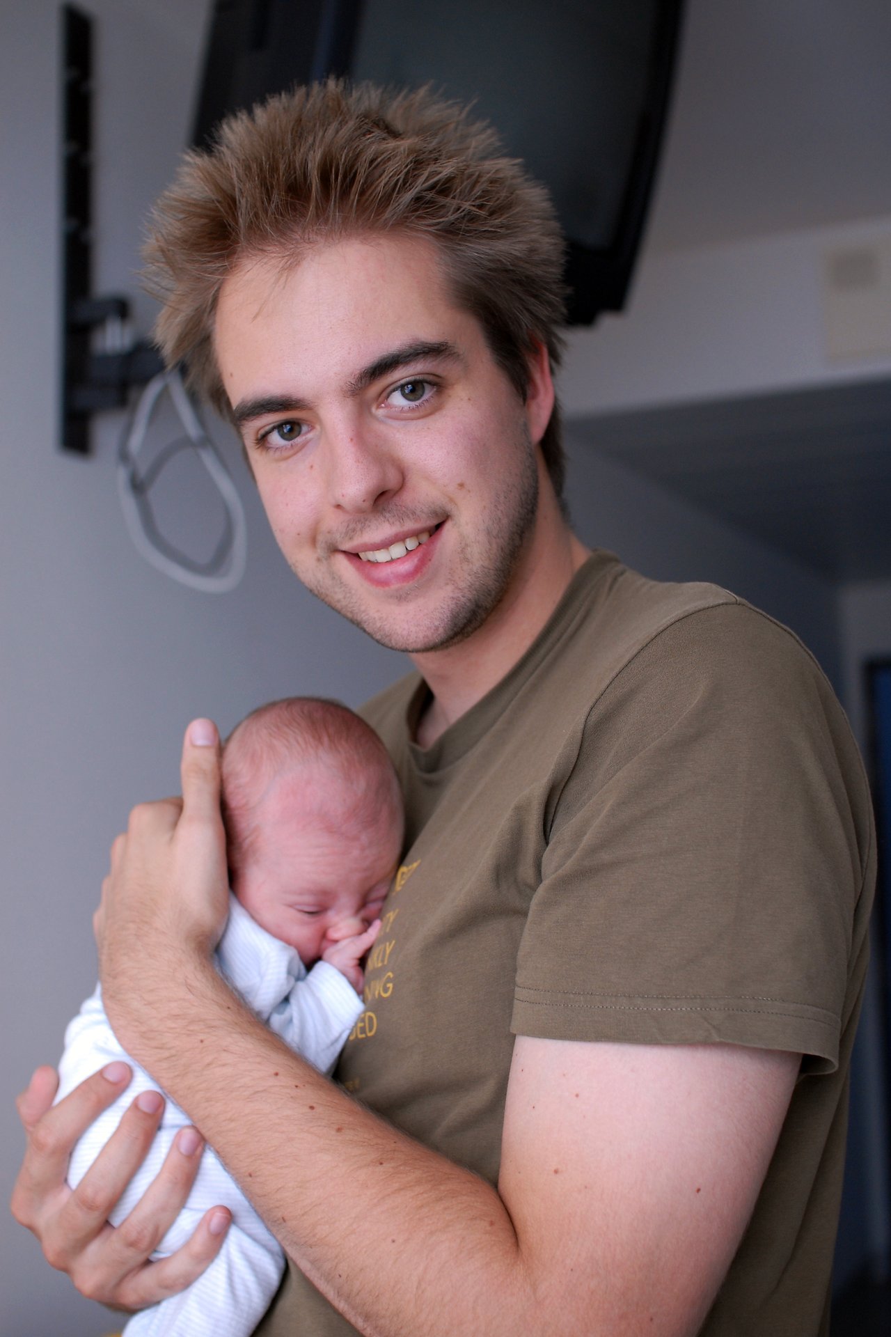 A man smiles while holding a newborn baby close to his chest in a gentle embrace.
