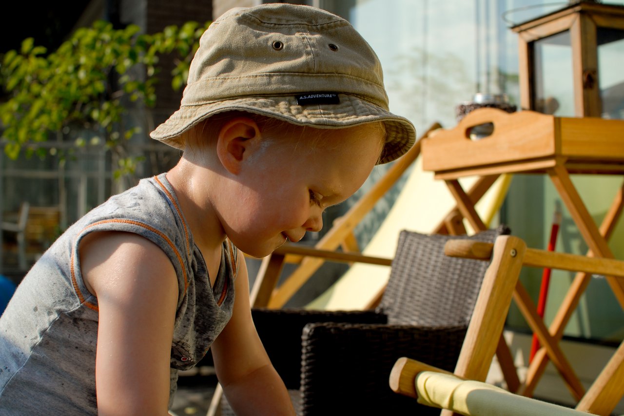 A young child wearing a hat and sleeveless shirt plays on a terrace, focused on an activity.
