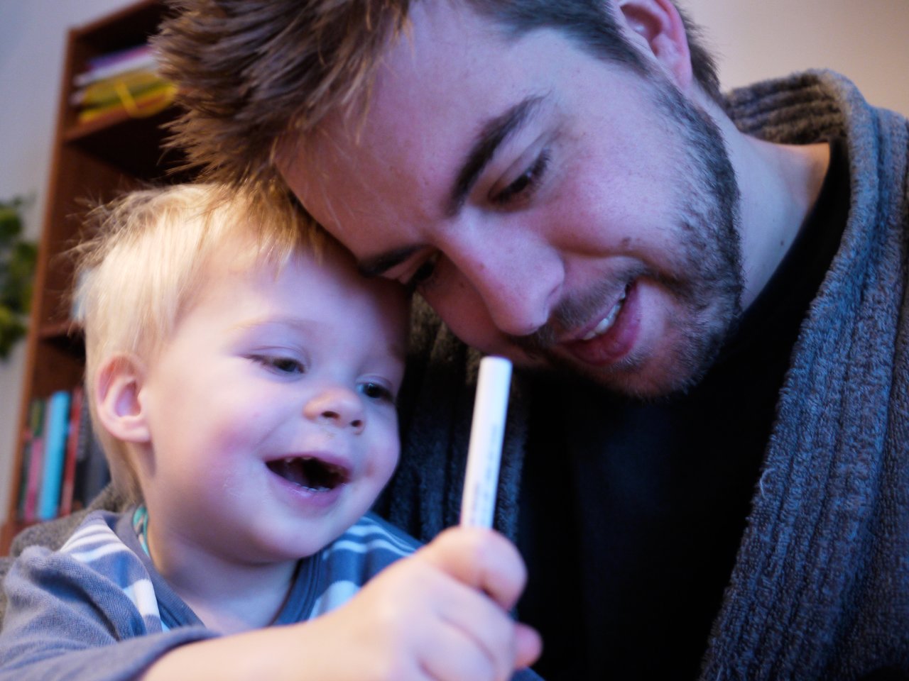 A child holds a pen while an adult watches closely, guiding them in learning to write.