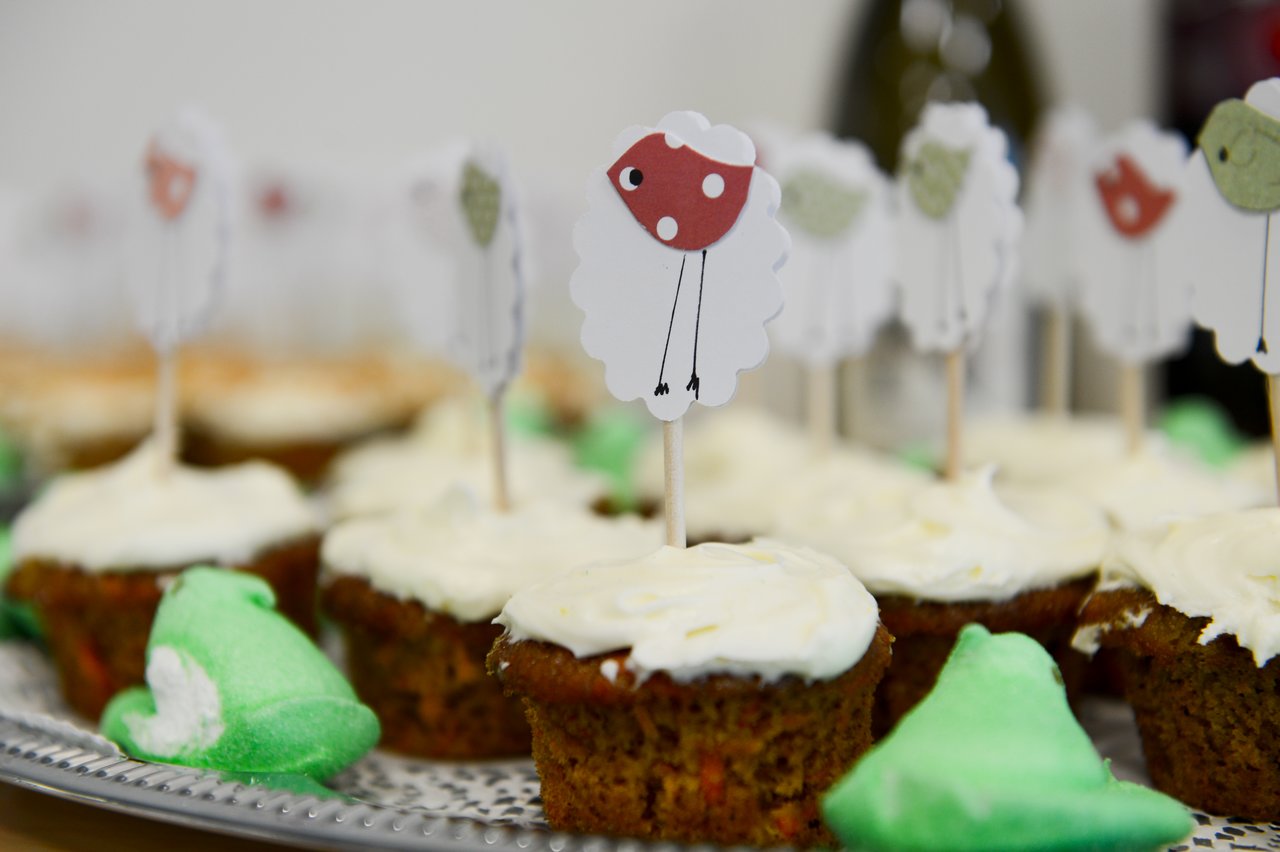 Cupcakes with white frosting, decorated with sheep and bird toppers on toothpicks, arranged on a tray for a baby shower.