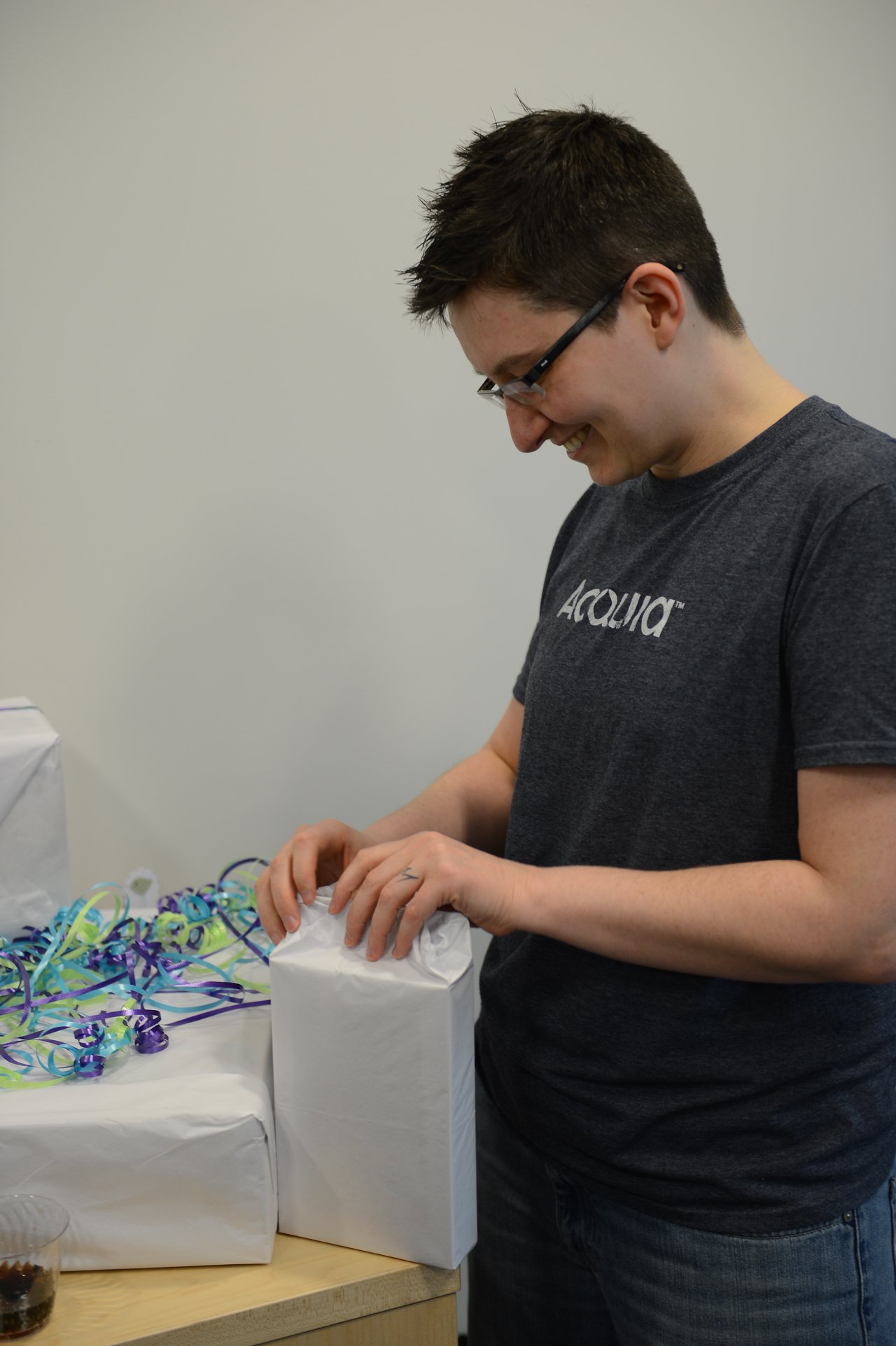 A person smiles while unwrapping a white gift at a baby shower.