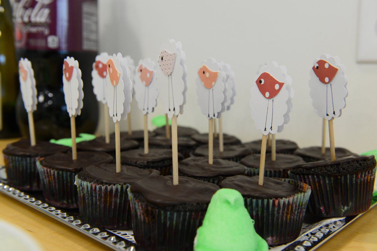 Chocolate cupcakes with sheep-themed toppers on a tray at a baby shower.